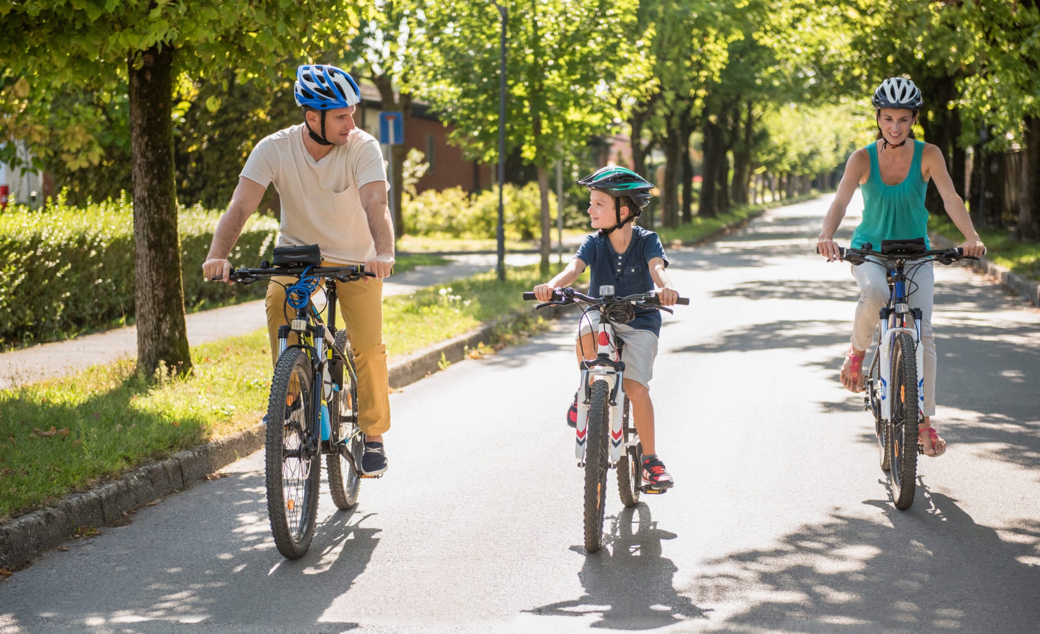 A man woman and a child ride their bikes down a treelined street.