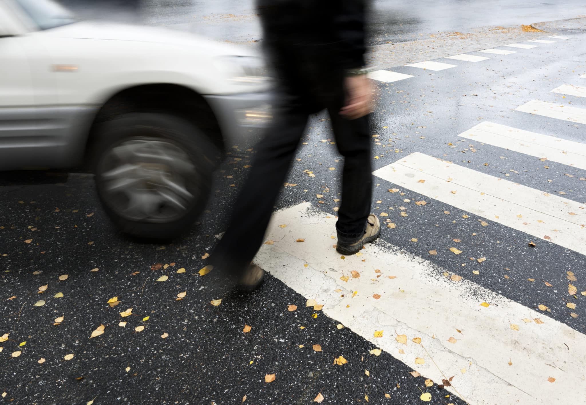 Pedestrian crossing street at a crosswalk with a white car about to hit him.