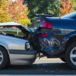 A side view of the smashed frontend of a silver car rearending a black car.