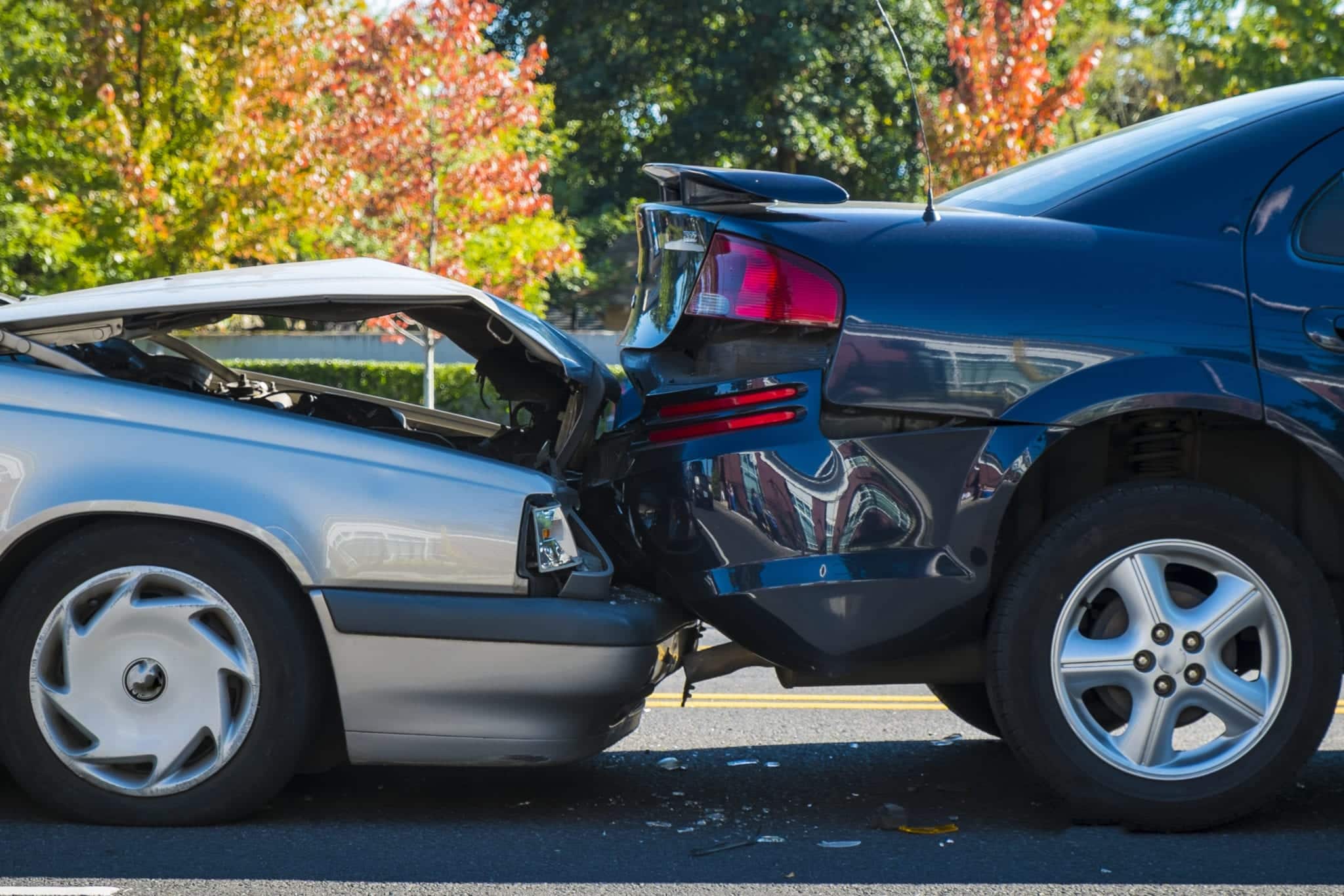 A side view of the smashed frontend of a silver car rearending a black car.