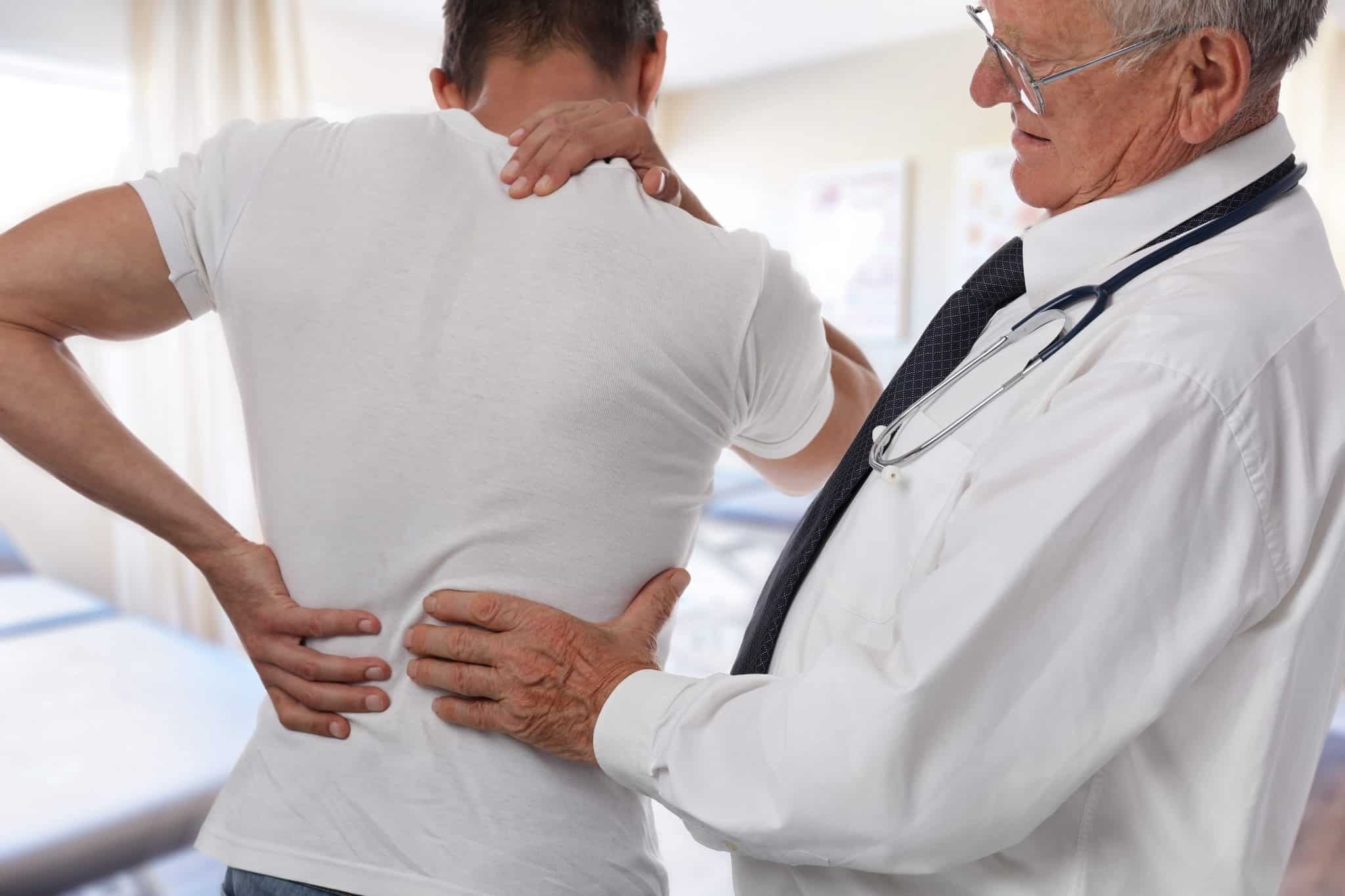 An older male doctor examining a male patient holding one hand on his neck and the other on his back.