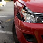 A closeup of a red car with a damaged right headlight after a car accident.