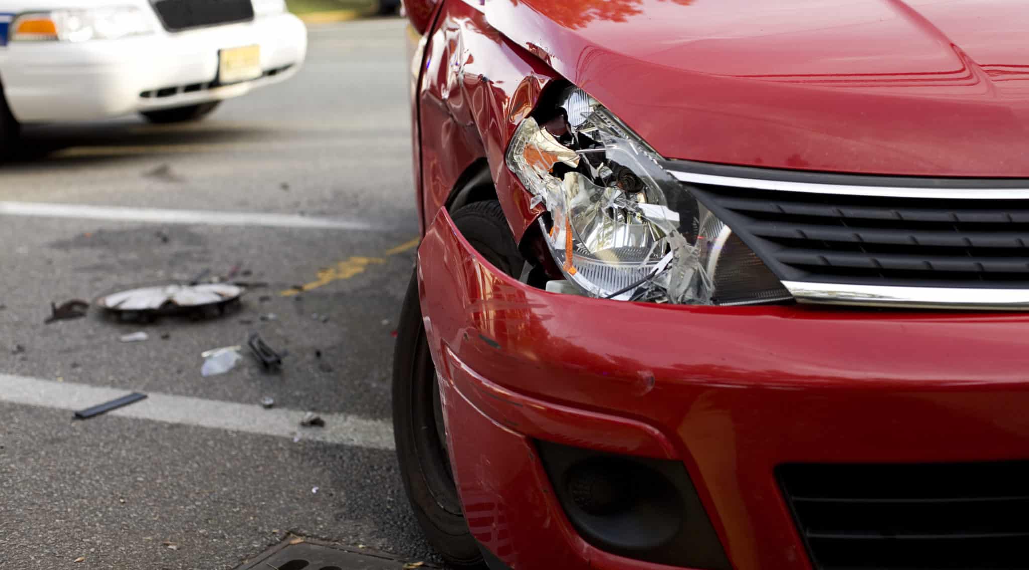 A closeup of a red car with a damaged right headlight after a car accident.