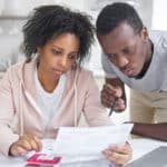 A stressed out couple sitting at a kitchen table and using a calculator to review bills.