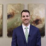 A male professional wearing a suit and standing in front of an abstract painting.