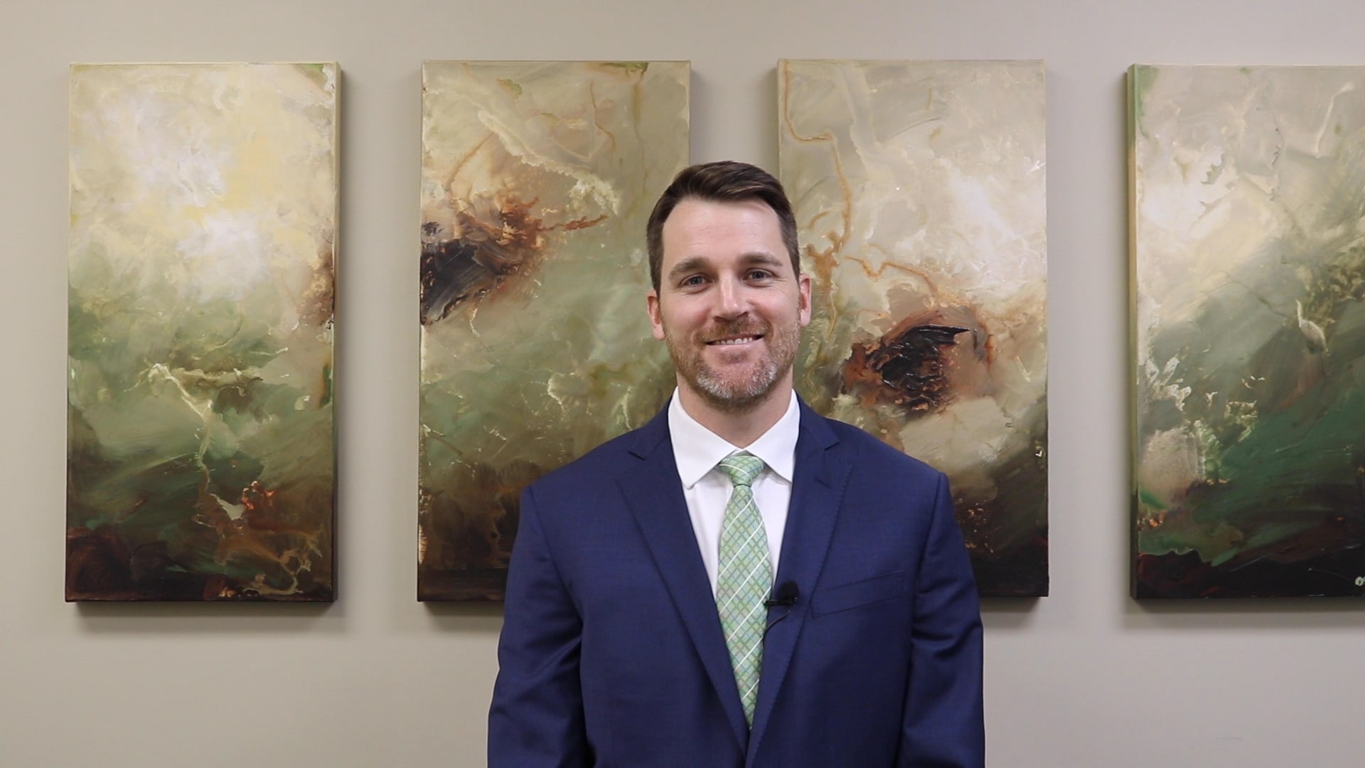 A male professional wearing a suit and standing in front of an abstract painting.