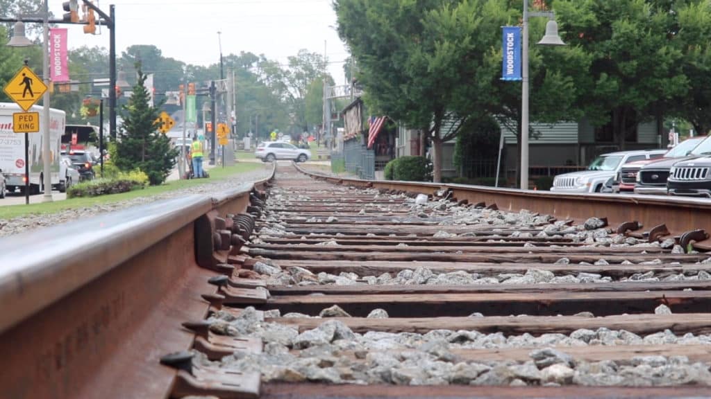 Close-up view of a railroad track showing cars, trees, and an intersection in the backgound.