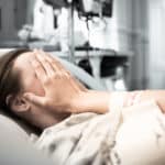 Female patient in a hospital bed holdong her face.