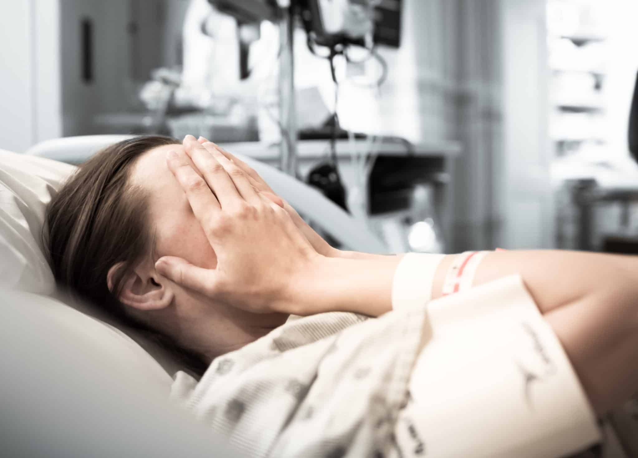 Female patient in a hospital bed holdong her face.