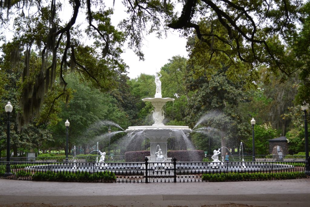 A large white fountain with a small black fence surrounding it.