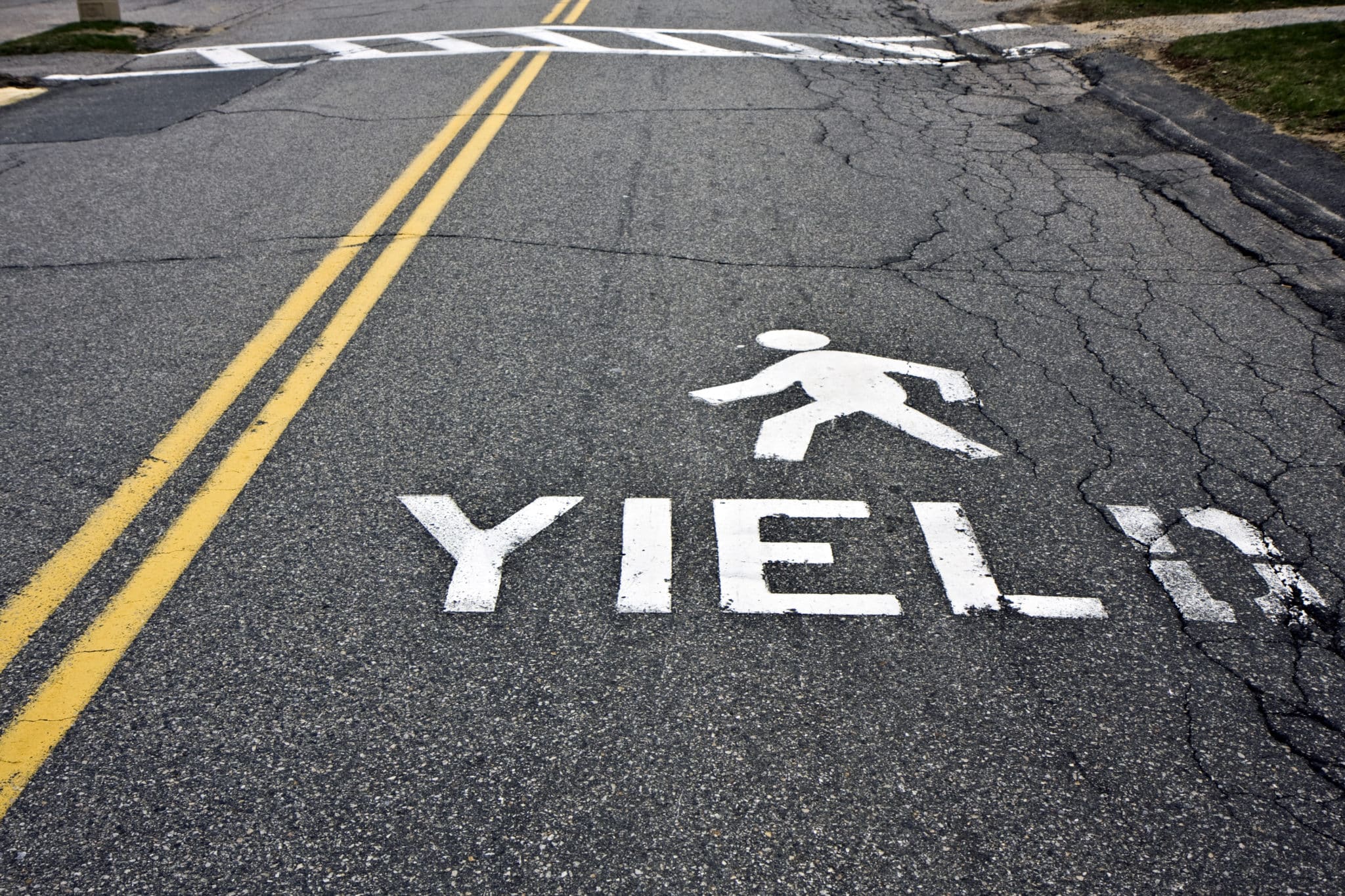 A stick figure painted on a road, walking across it about the word YIELD.