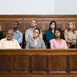 A group of ten women and men, all looking toward their right, sitting in a woodedn jury box.