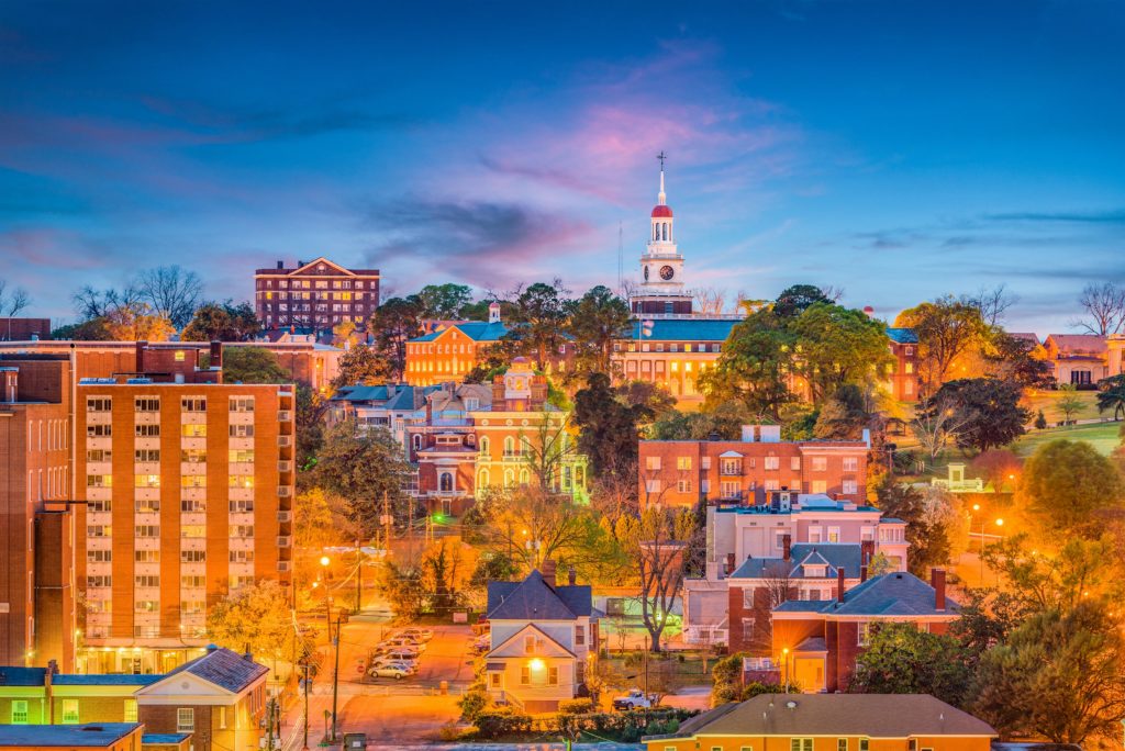 An aerial view of Macon, Georgia at dusk with the buildings appearing in a warm orange light againts a dark blue sky.