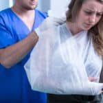 A doctor wearing blue scrubs tieing a white sling around a woman's right arm.