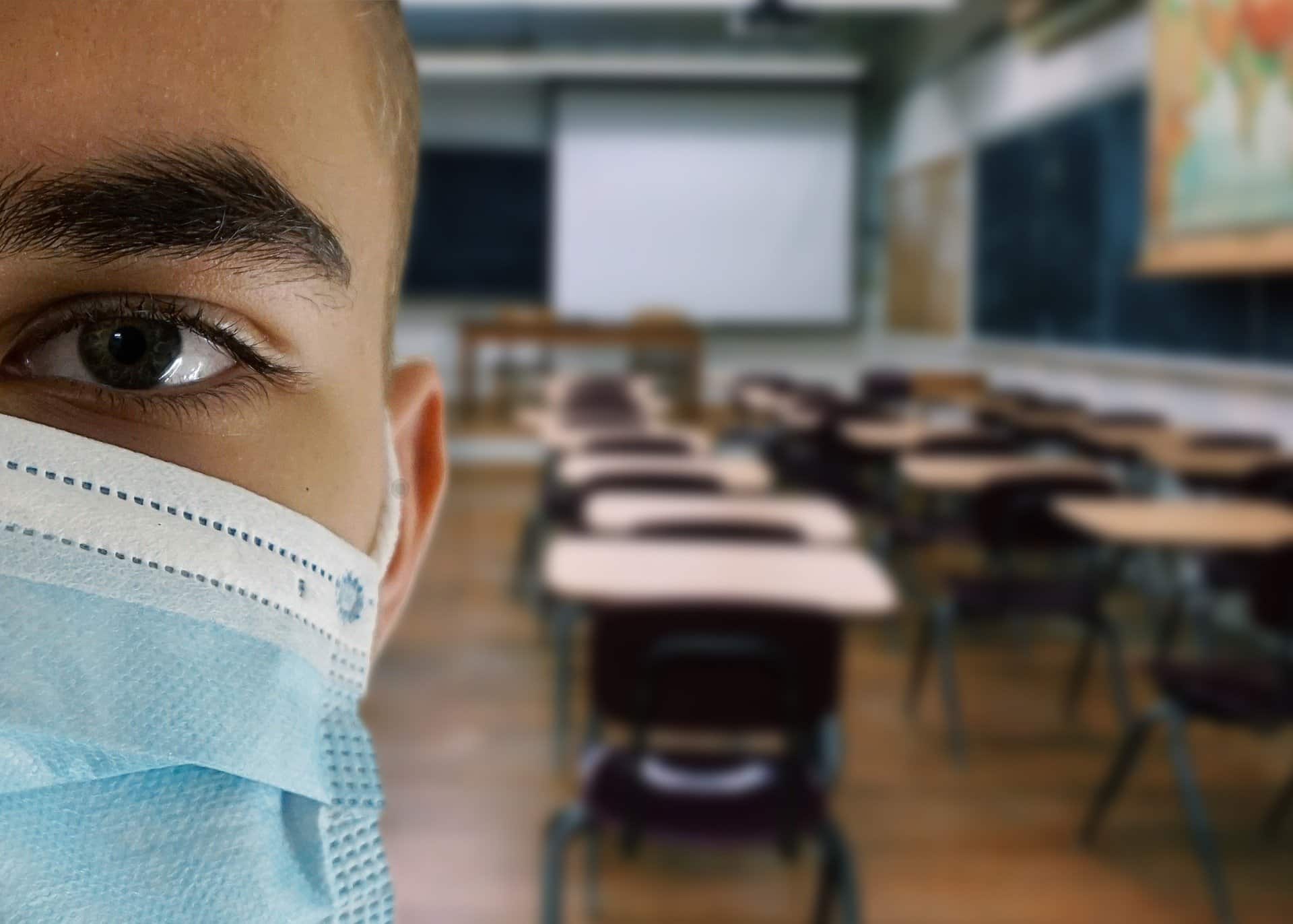 Close-up of a kids face wearing a blue face mask in front of a blurry view of a classroom in the background.