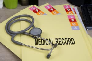 Yellow folders with the words medical record on them and a stethoscope laying on top of the folders.