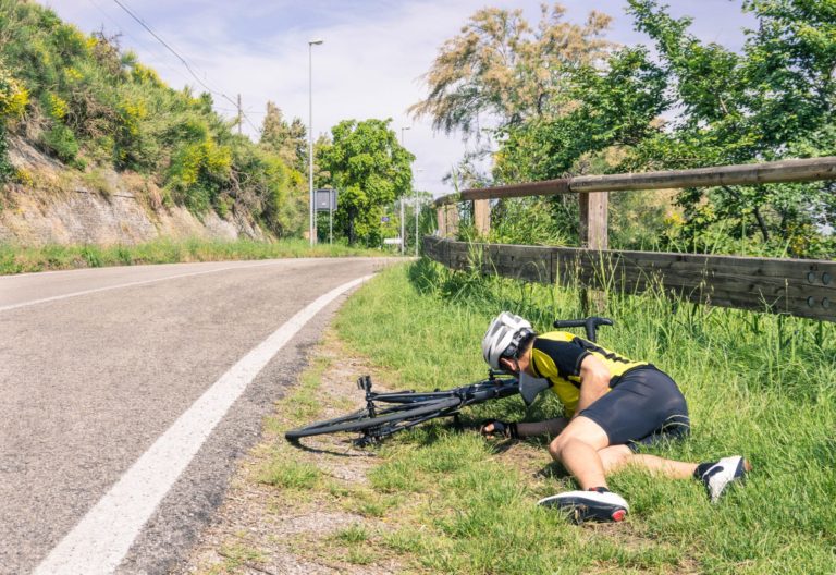 Male cyclist lying in the grass on the side of the road after falling off his bicycle.