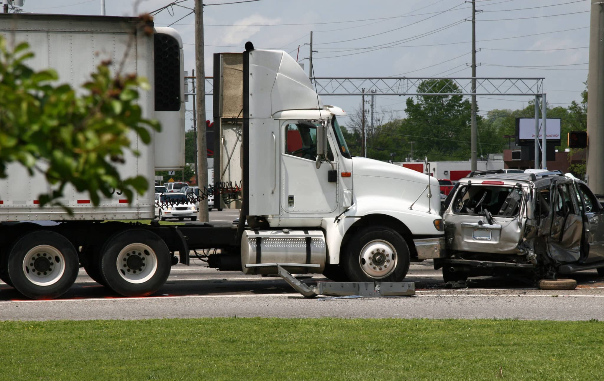 A white tractor trailer in a wreck with a silver car that has sustained severe damage.