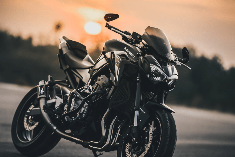 A black kawaski motorcycle parked infront of the sun setting below the trees.