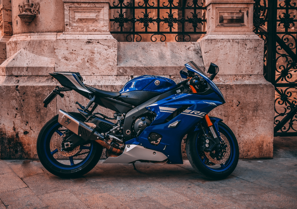 A blue motorcycle parked in front of a large stone wall with a metal gate in the middle.