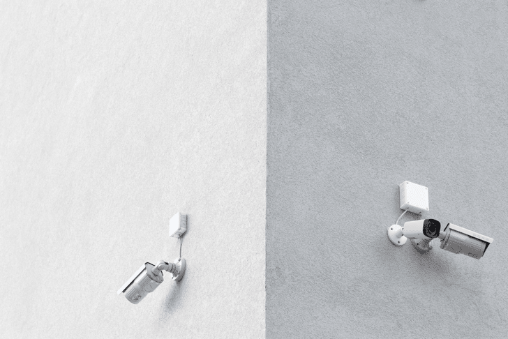 A corner of a white building with security cameras on both sides.