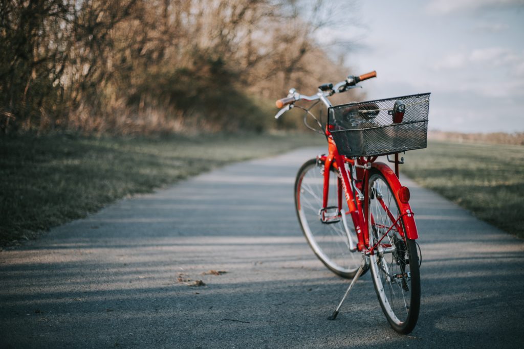 The back of a red bicycle with a basket on the back parked on a bike path.