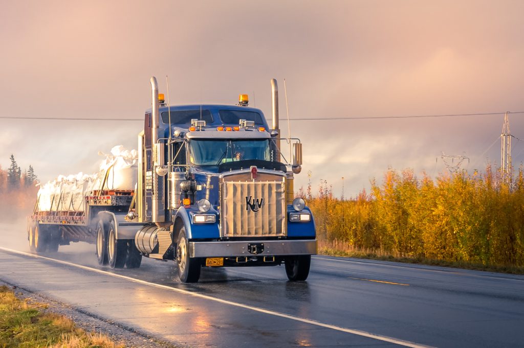 The front end of a blue tractor trailer driving on a wet road.