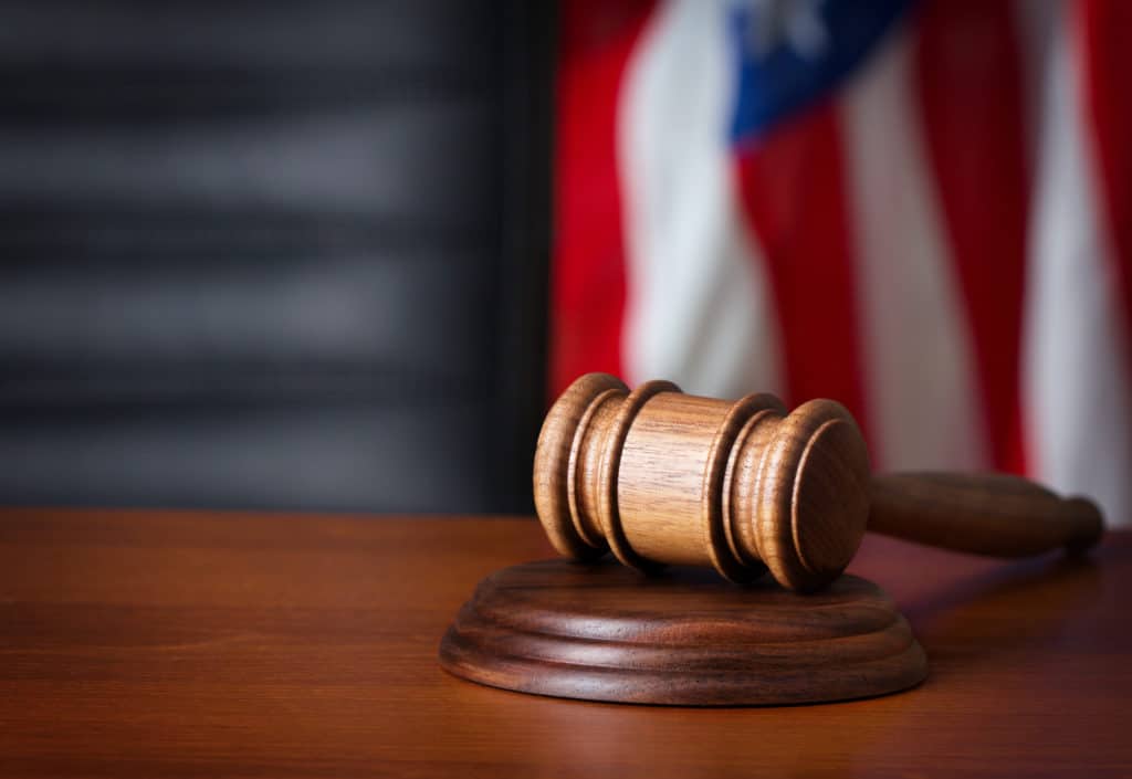 A closeup of a gavel with a blurred image of the American flag in the background.