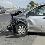 Aftermath of a car crash showing a silver car with the front end smashed in.