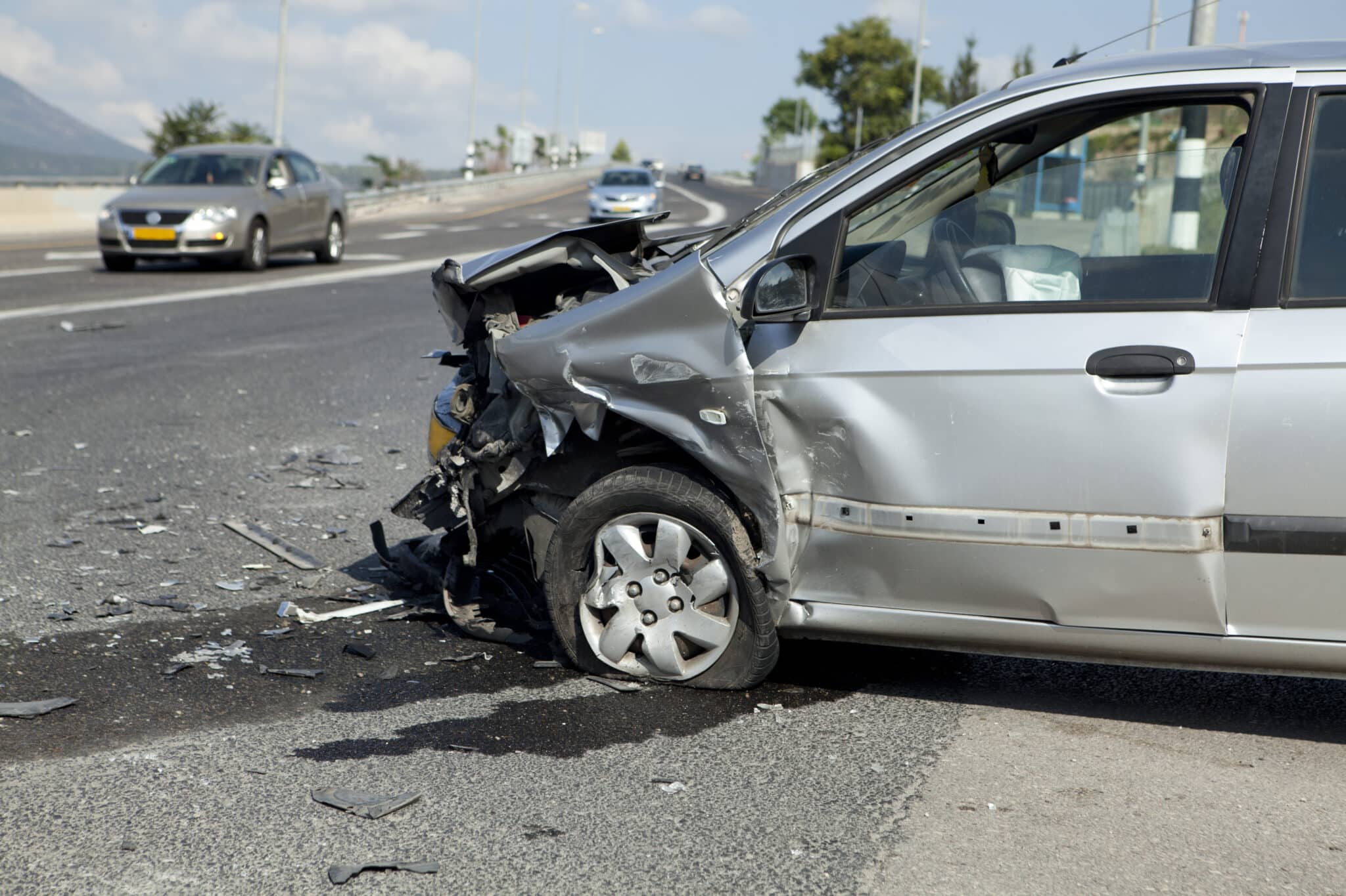 Aftermath of a car crash showing a silver car with the front end smashed in.