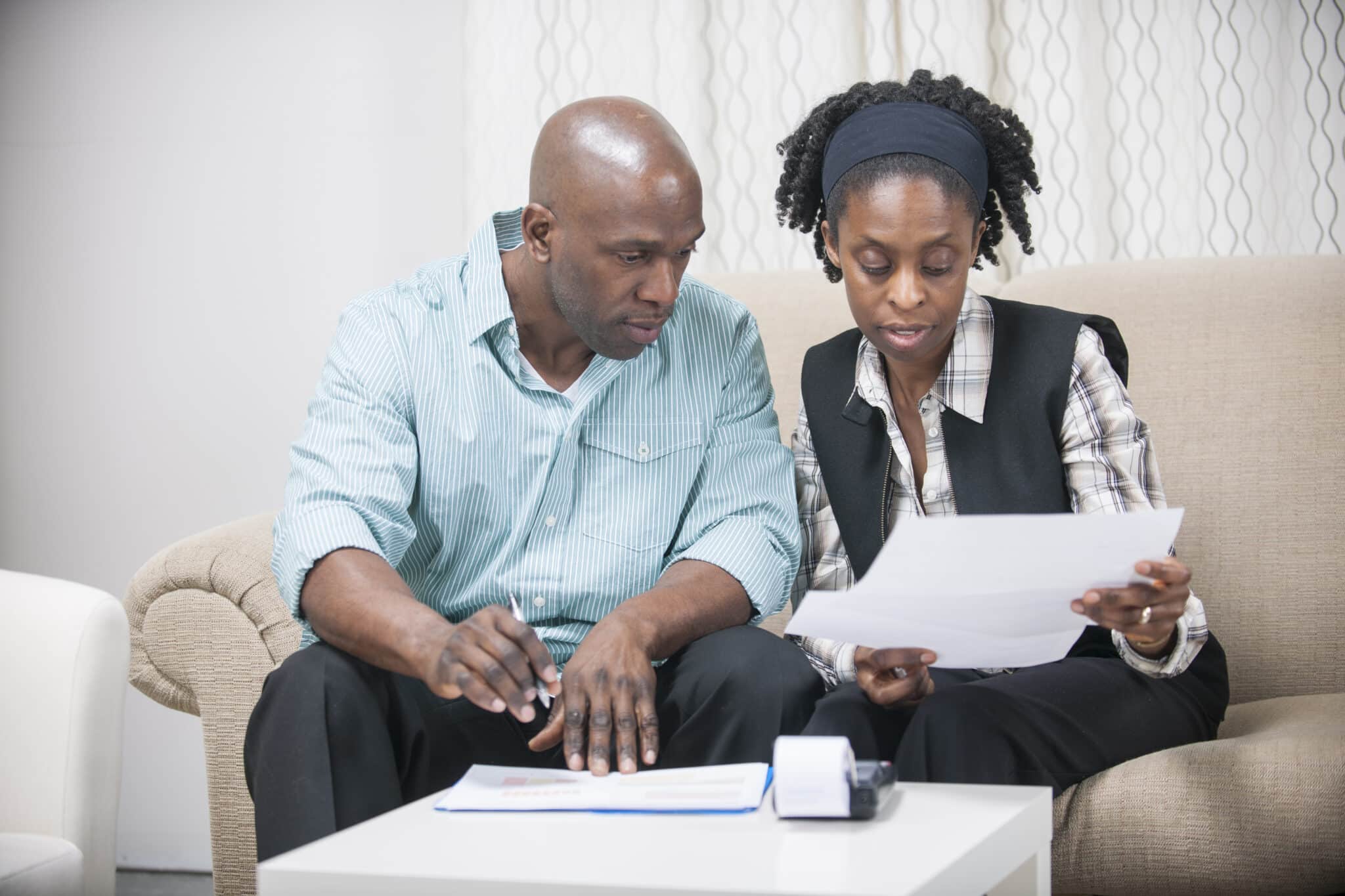 Couple sitting next to each other on a couch discussing documents.