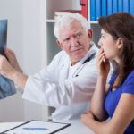 A male doctor holding up an x-ray, pointing something out to a surprised female patient.