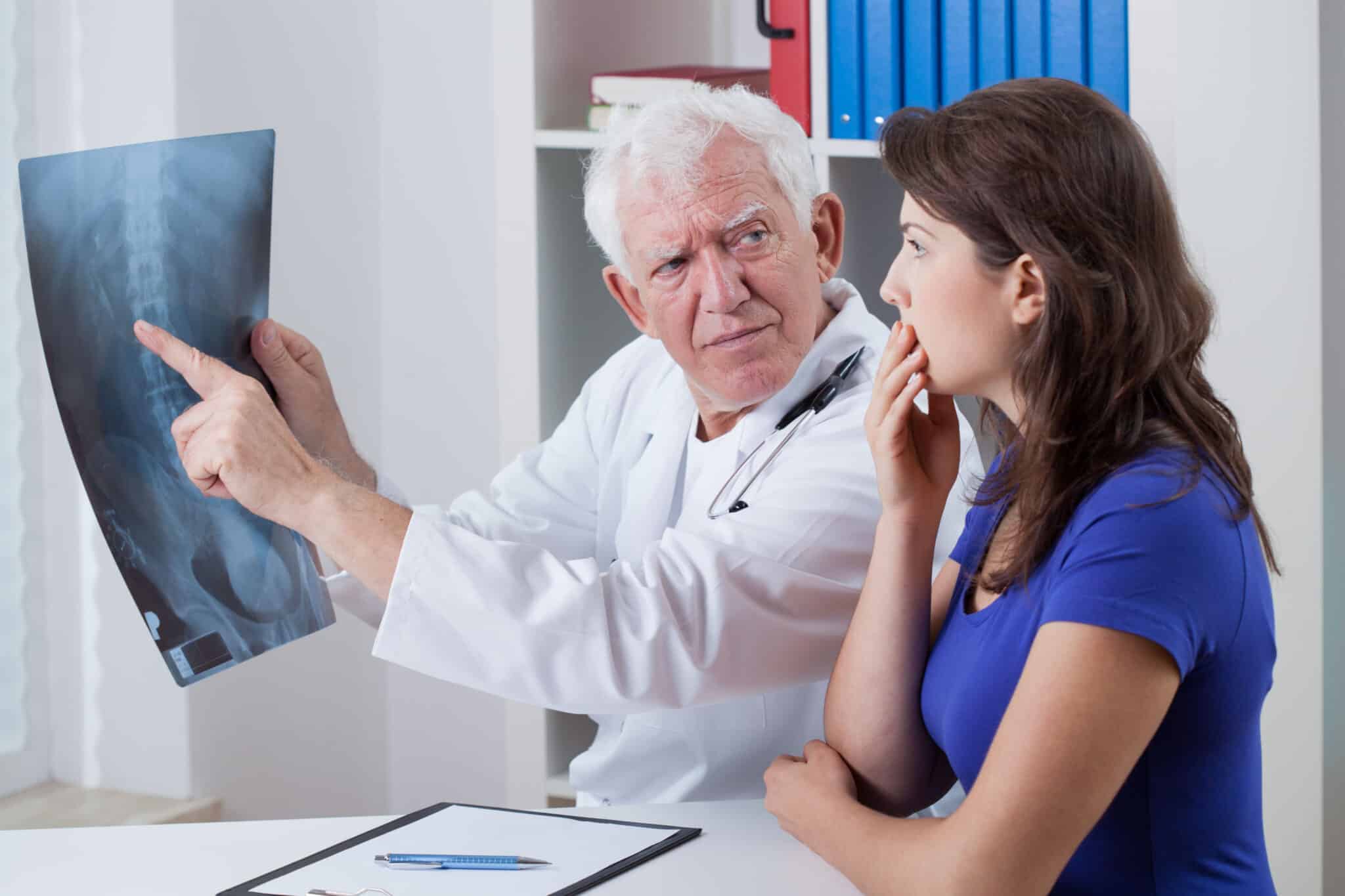 A male doctor holding up an x-ray, pointing something out to a surprised female patient.