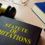 A gavel, eye glasses and a book with the title, Statute of limitations, on a desk.