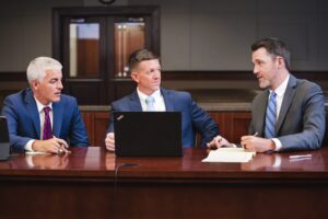 Three attorneys having a discussion while sitting at a desk in a courtroom.
