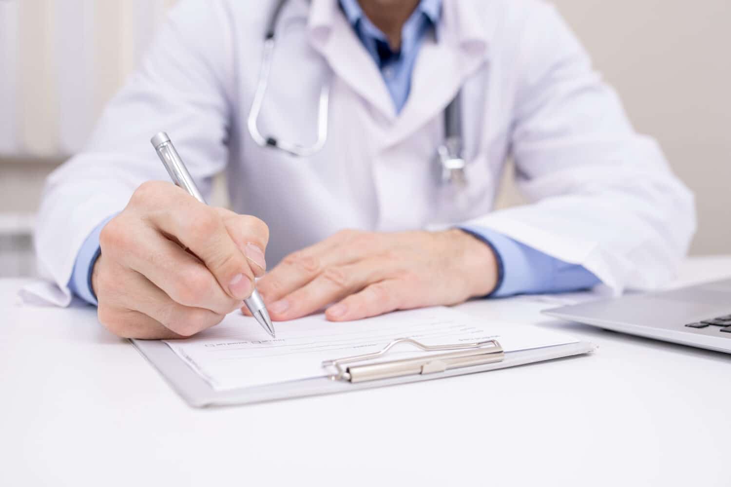 A doctor sitting at a desk,writing on a clipboard.