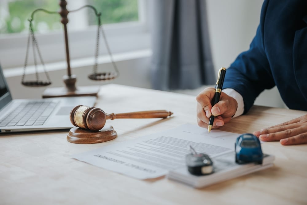 Male judge’s hand holding a gavel beside a toy car and legal documents, symbolizing car accident law and legal proceedings