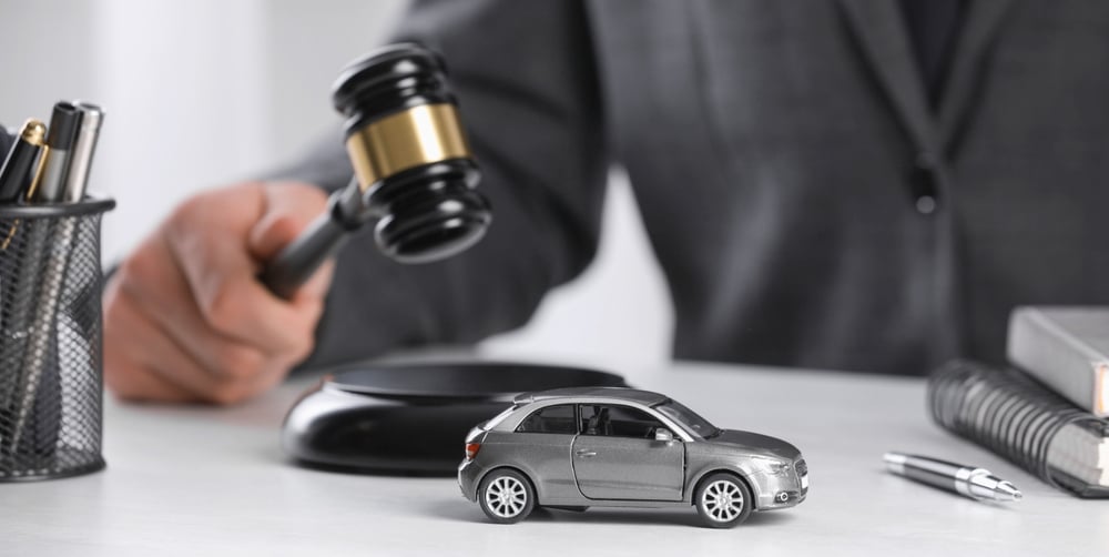 Close-up of a judge striking a gavel on a table with a toy car in focus, used as a banner design concept for legal matters involving vehicles.