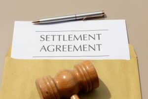 Settlement agreement document placed on a wooden desk beside a judge’s gavel, symbolizing the final resolution of a legal case.