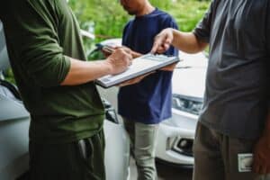 Three Asian men meet with an insurance adjuster to discuss car insurance policies, reviewing premiums, deductibles, coverage, and a recent claim settlement.