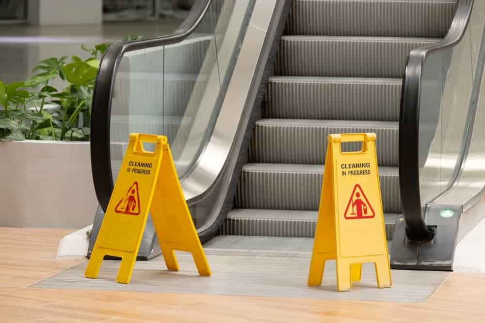 Two yellow caution signs are placed on the steps of an escalator. The signs warn people to be careful while using the escalator