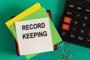 RECORD KEEPING - words on note paper against the background of a calculator and paper clips
