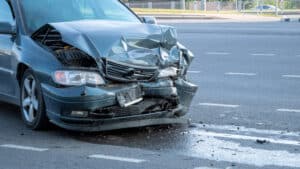 Car with severe front-end damage after a collision on a city roadway.