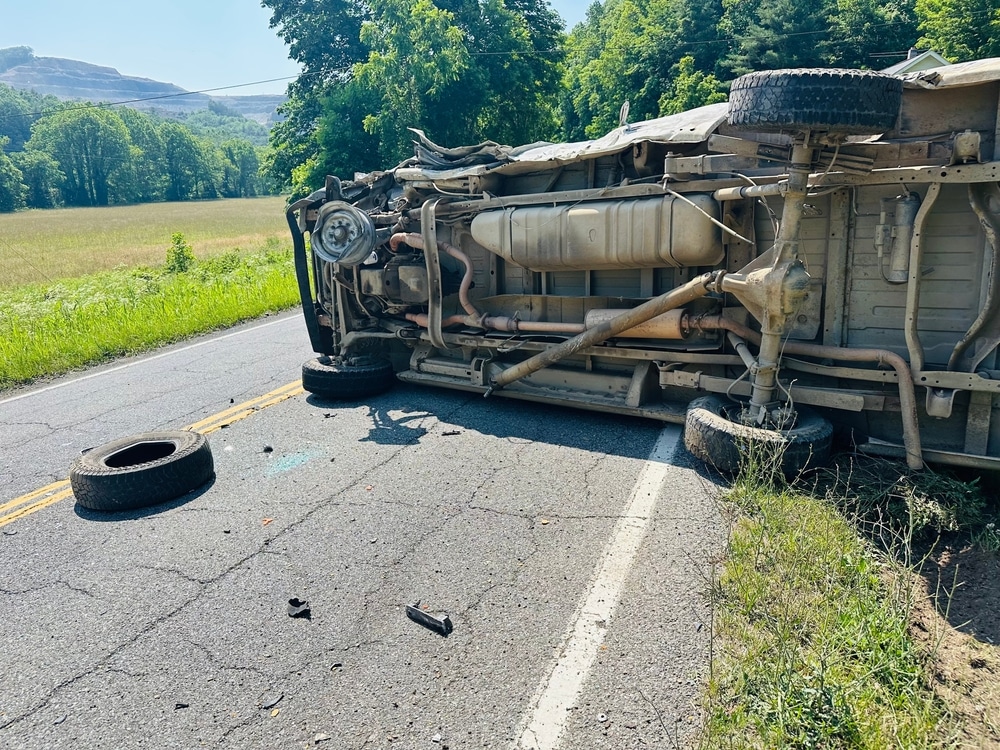 Overturned commercial truck on a rural road with debris scattered across the pavement.