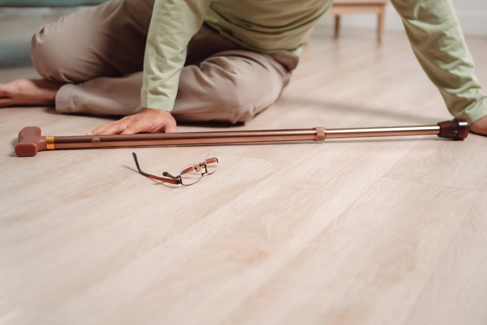 Elderly person on the floor after a fall with a cane and eyeglasses lying nearby