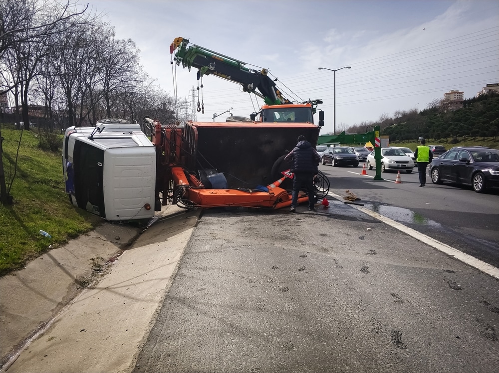 Rollover truck accident with tow crews working at the scene on a busy highway.